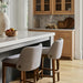 Two light gray upholstered bar stools with wheat-finished beechwood bases at a kitchen island.
