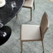 Surya Eric Dining Chair with light brown PVC upholstery and khaki iron base next to a black marble table.