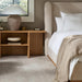Beige upholstered bed with a tall headboard, white bedding, and a beige knitted throw.
