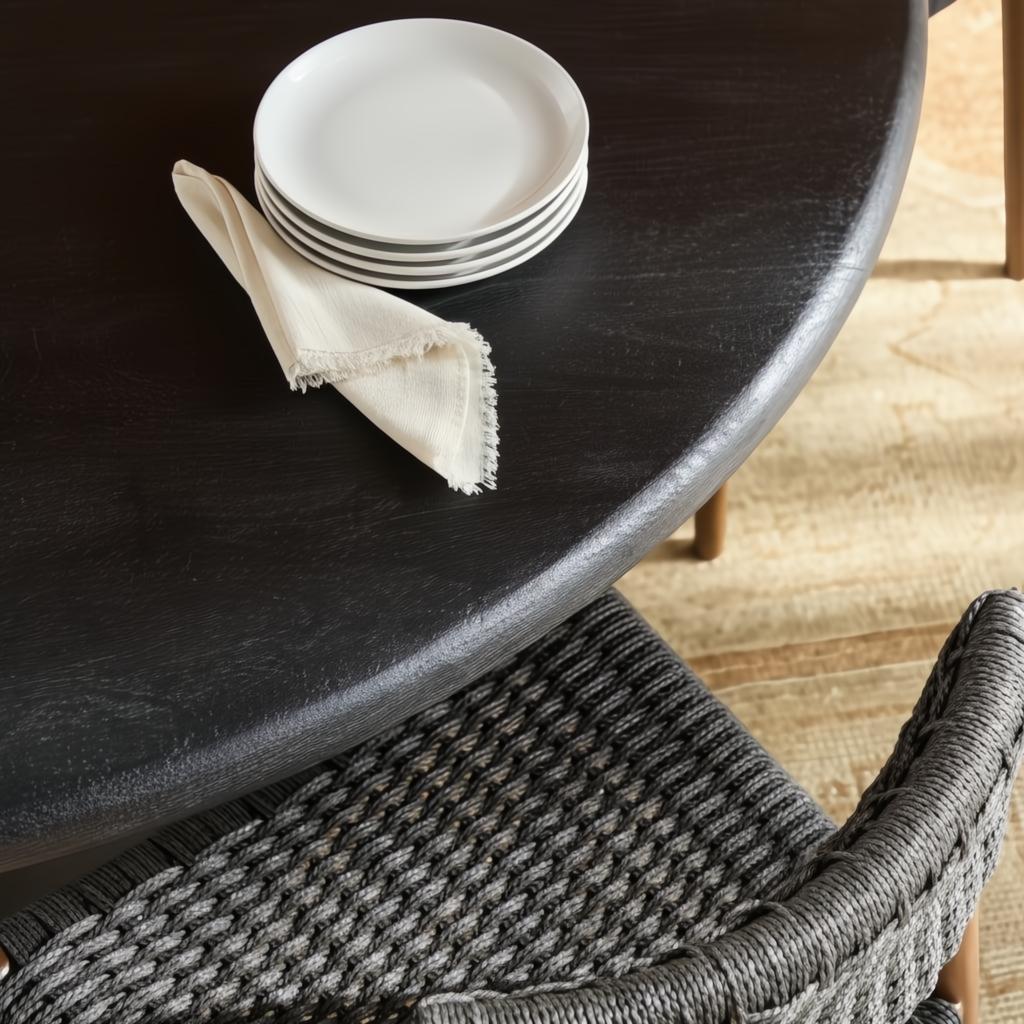 Black brushed mango wood dining table with a round top, white plates, and a linen napkin.