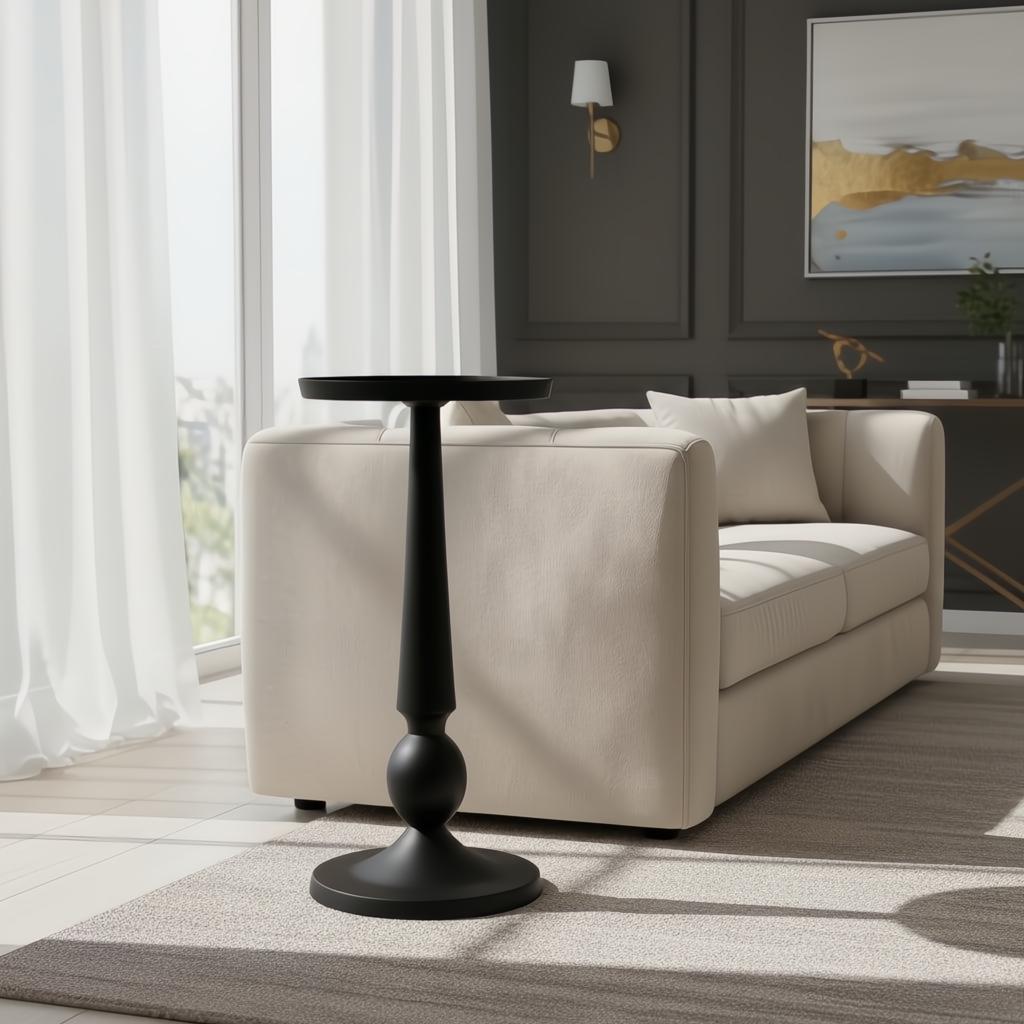 Black aluminum Surya Molino End Table with a pedestal form, 21"H, beside a beige sofa.