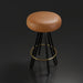 Surya Oberon backless bar stool with brown leather seat, black steel legs, and a brass footrest.