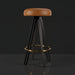 Surya Oberon backless bar stool with brown leather seat, black steel base, and gold footrest.