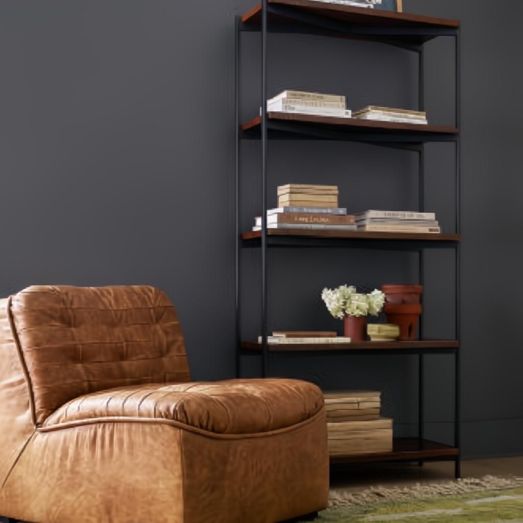 Surya Oryan modular chair in brown leather with a black rubber wood base, next to a tall bookshelf.