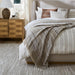 Surya Covina upholstered bed with a light brown headboard, striped bedding, and a fringed throw.